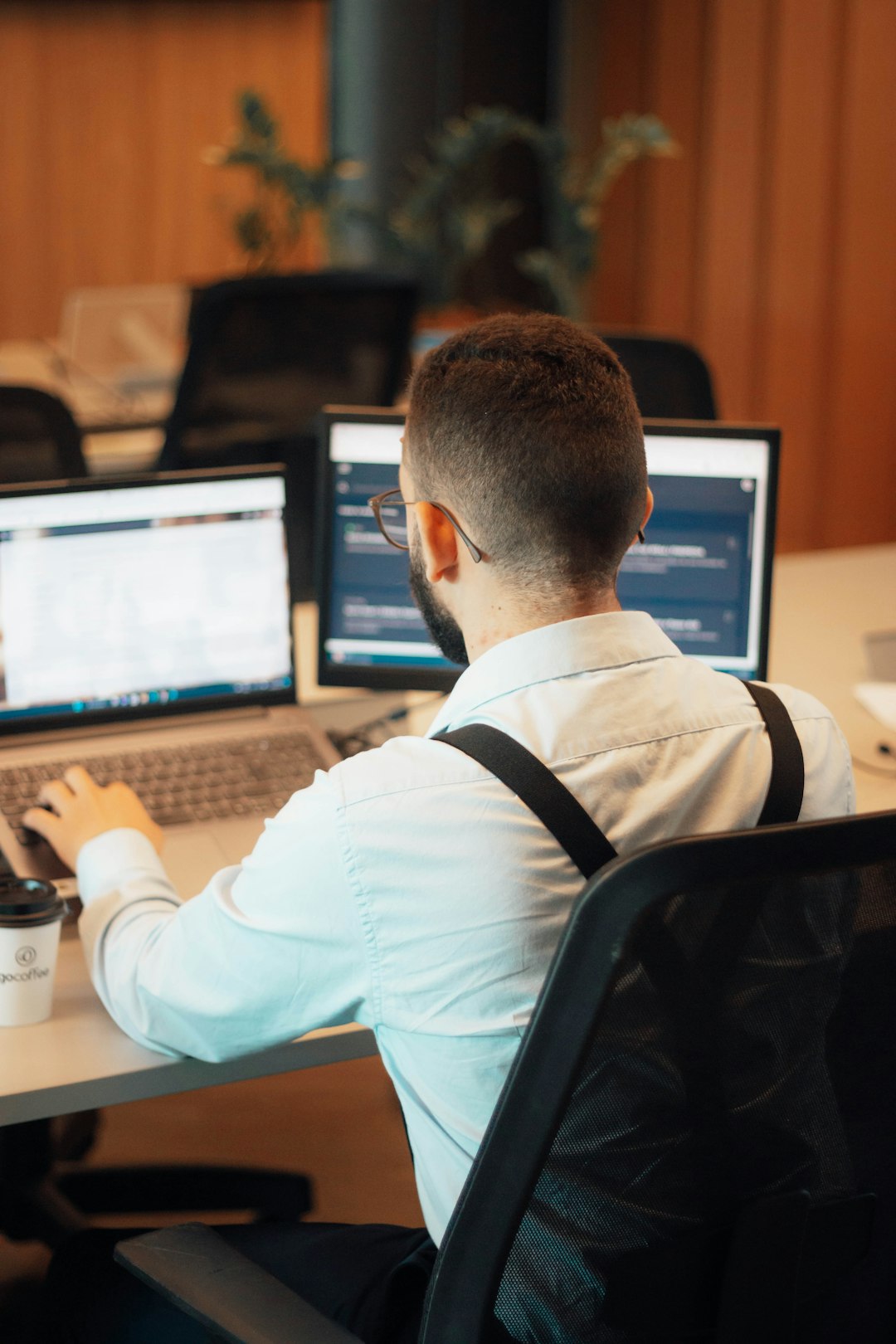 a-man-sitting-at-a-desk-with-two-laptops-f74htpflhr8
